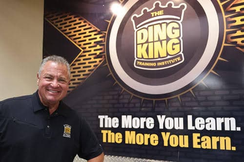 Todd Sudeck, President and Founder of The Ding King Training Institute, in front of the Ding King mural reading "The More You Learn. The More You Earn."